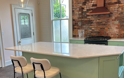 kitchen with mint green cabinets, white counter, and exposed brick wall